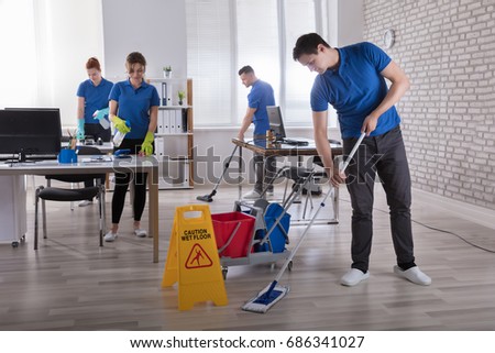 Group Of Janitors Cleaning The Modern Office With Caution Wet Floor Sign