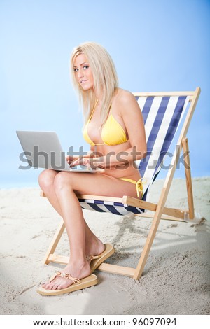 Beautiful young woman in bikini lying on a deckchair using laptop at the beach