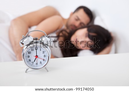 Close-up on alarm clock and lovely young couple on background