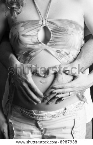 Father making heart shape on mother's belly with mother's hand