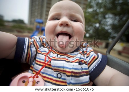 six months -old girl on a swing in the playground - show her tongue