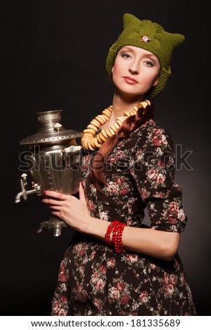 Girl in soviet retro style posing with samovar. Girl with a green cap on his head. Star on the cap.