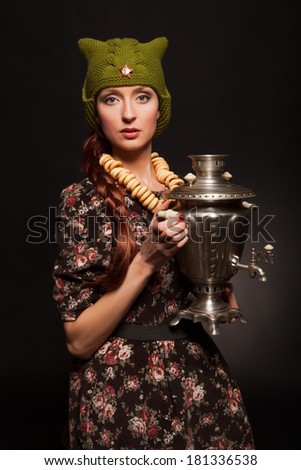 Girl in soviet retro style posing with samovar. Girl with a green cap on his head. Star on the cap.