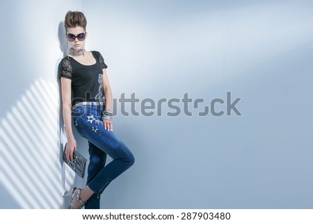 fashion shot of girl with sunglasses holding purse posing in light background