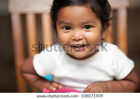 excited baby girl holding a spoon and sitting on a booster seat