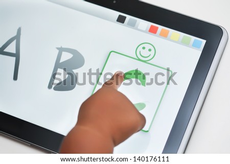 The finger of a toddler selecting the correct letter on a touchscreen tablet with learning software.