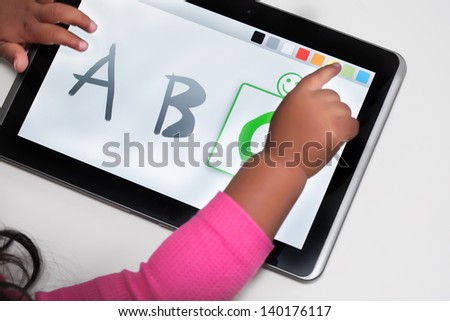 The hand of a child on a touchscreen tablet with educational software.