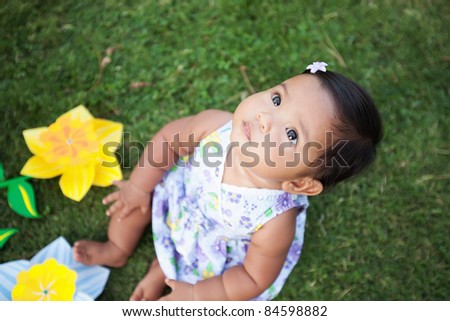 Cute baby girl looking up at the sky sitting on the lawn with pi