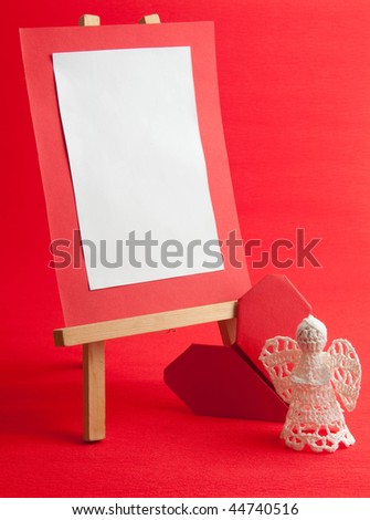 wooden easel with blank card, angel and paper heart on red background