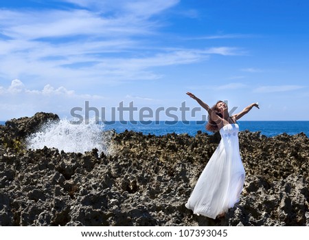 Beautiful bride with eyes closed standing on reefs near the ocean