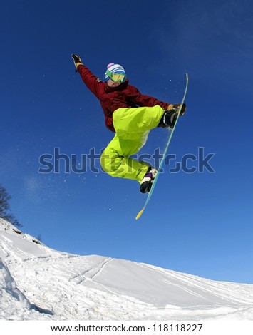 Jumping snowboarder keeps one hand on the snowboard on blue sky background