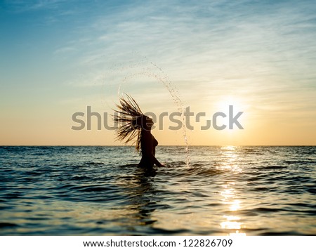 Silhouettes of young woman jumping in ocean at sunset