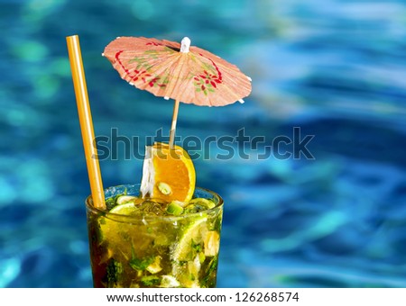 Glass of ice cold cocktail mojito with umbrella near swimming pool