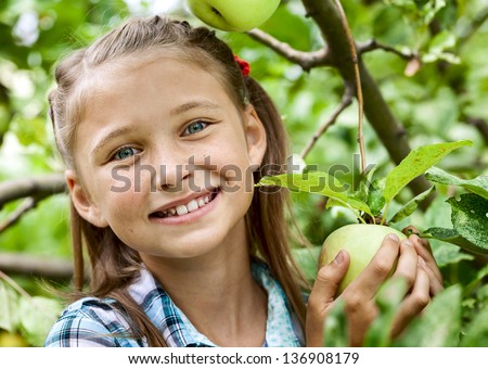 Smiling young girl collects the apples from tree