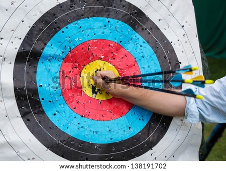 A man\'s hand pulls arrows from hitting 10 points. Standard colorful target for archery.