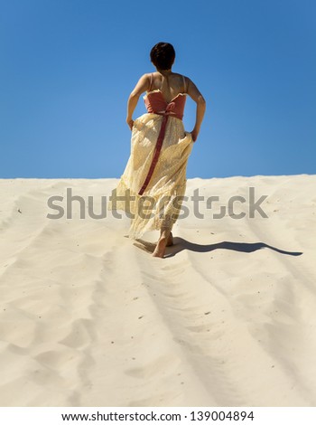 Silhouette of lonely young woman walking on sand in desert
