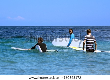 Three surfer enter into the ocean with surf boards to the starting point for riding on the waves