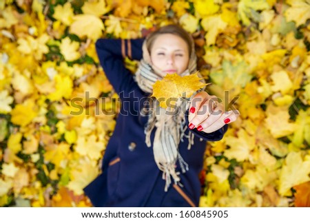 Happy young woman lying down resting and dreaming in autumn leaves. Top view