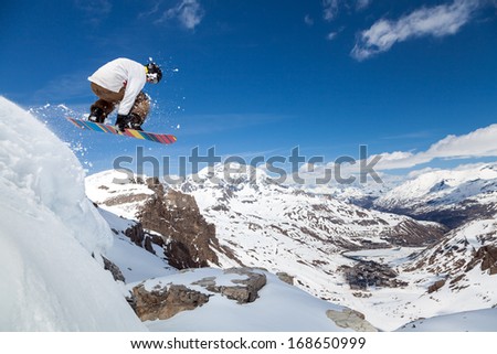 Jumping Snowboarder Keeps One Hand On The Snowboard On Blue Sky Background