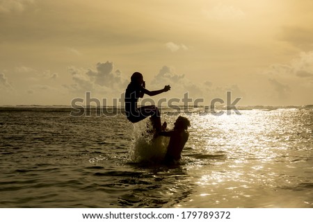 Silhouette of young girl jumping out of the ocean, which throws strong two man on the background of the expiring sunset. Single shooting