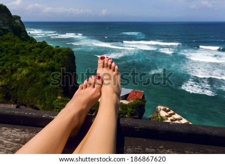Closeup of beautiful female legs hanging on background of mountains and ocean scenery