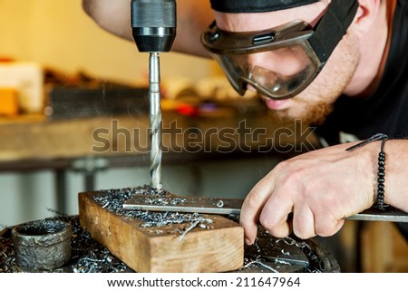 Electric drilling machine with manual pressure, a man holding a metal part and the hole is drilled, strongly pressing drill to the workpiece surface