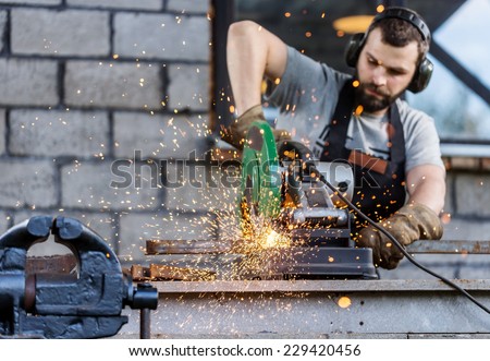Industrial worker cutting metal with many sharp sparks working on compound mitre saw with circular blade