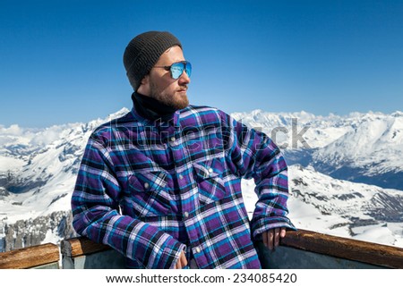 Portrait of young man in sunglasses at ski resort in the background of mountains and blue sky