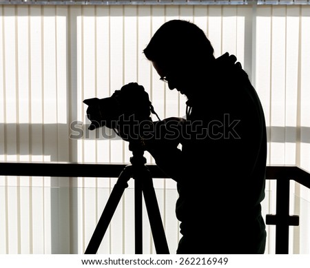 Silhouette of photographer and cameraman shot the video on a tripod at the workplace indoors