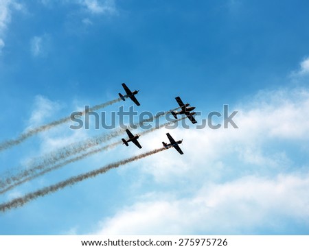 Silhouette sport aircraft with propellers, performing tricks with a smokescreen against the blue sky in the air show performance