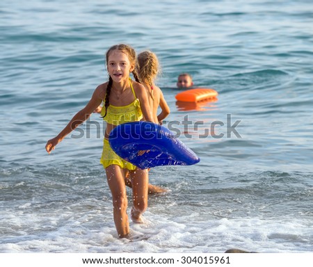 Happy little girl runs out of the sea on the beach with inflatable pillow
