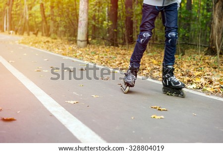 Teenager in motion on roller skates with protection on the knees in autumn park and special track for ride