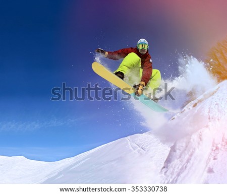 Jumping snowboarder keeps one hand on snowboard in mountains in ski resort on blue sky background