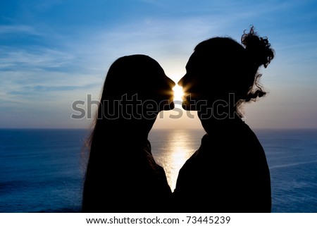 Silhouette of a young couple kissing at the beach with the sun setting behind them