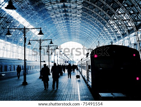 Covered railway station with trains and silhouettes of hurrying people