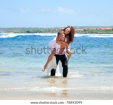 Portrait of young man carrying his cute young girlfriend on his back. The happy couple comes out of the ocean