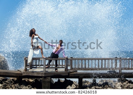 Happy young couple walking on the old pier. Ocean waves beating on the rocks