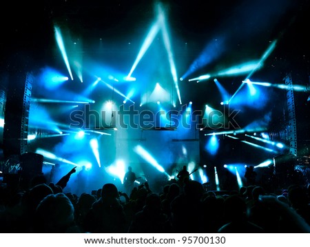 Silhouettes of people and musicians in big concert stage. Bright beautiful rays of light