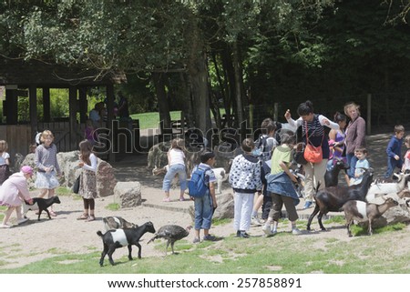 LISIEUX, FRANCE - JUNE 29, 2011: Group of children and adults in petting zoo of Zoo de Cerza in Lisieux, France. A woman and some children are afraid of the naughty and intrusive goats.