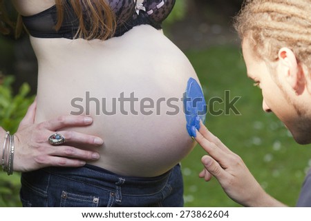Young Man finger painting on a woman\'s pregnant belly -  Germany, Europe