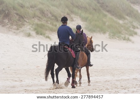 BERGEN AAN ZEE, NETHERLANDS - SEPTEMBER 11, 2005: Father and daughter riding horses on the beach. This beach is well known for the large dunes running parallel to the shoreline.