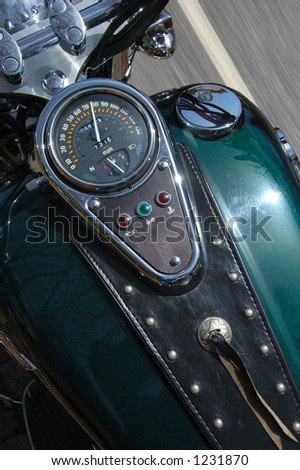 Motorcycle viewed from driving position apparently moving down a highway.  Road, whiteline visible.  Speedometer says 75.  Close to empty on gas gauge.  Specular highlights in chrome and paint