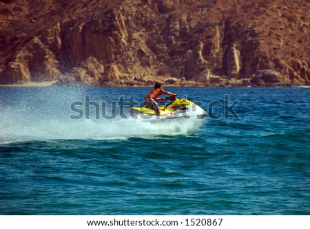 Man on wave running motor boat.  He moving very quickly.  There is a large spray of water behind the boat.  The water is deep blue.