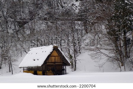 Winter scene in Japan.  There is a wooden house called a Gasho.  There are snow covered trees visible.