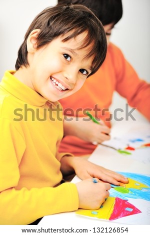 Two little kids at the table draw with crayons and smiling