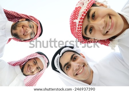 Happy group of Arabic people with heads together in circle over sky background