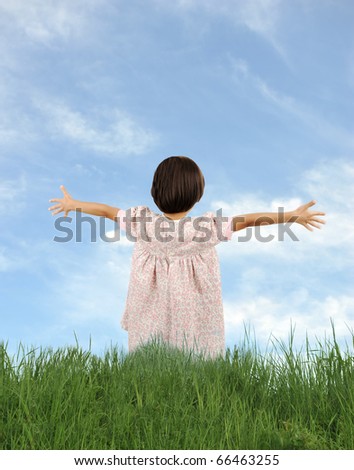 Happy little girl with wide opened arms, on grass in nature, blue sky background: bright future and freedom