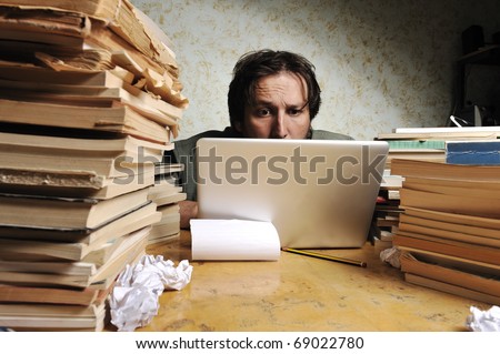Businessman working in office on laptop. Messy table with a lot of books on.