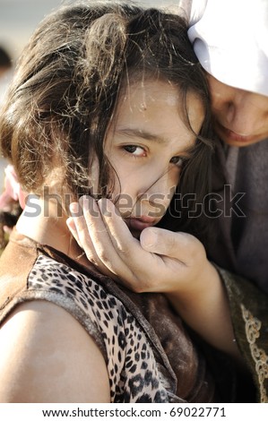 Poverty and poorness on the children face. Sad little girl. Refugee. In Muslim  mother\'s arms.