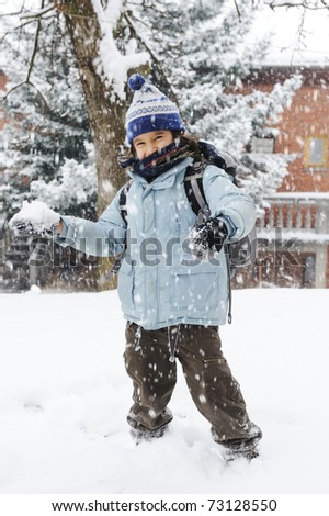 happy schoolboy kid wearing warm clothes in snow on a cold winter day, smiling and joying